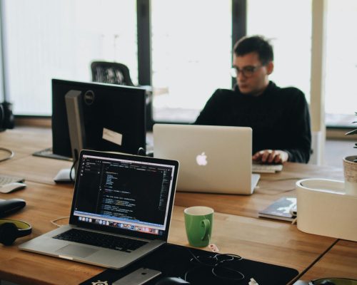 A web developer working on code in a modern office setting with multiple devices.